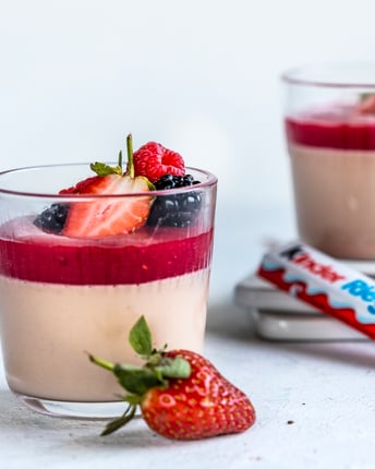 Zwei Gläser mit Panna Cotta und Himbeermark auf weißem Tisch mit angelegtem Kinder Riegel
