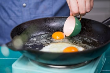 Das Ei wird mit einer Tasse in eine Pfanne gegeben