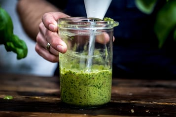 grünes Pesto wird in einem durchsichtigen hohen Gefäß püriert