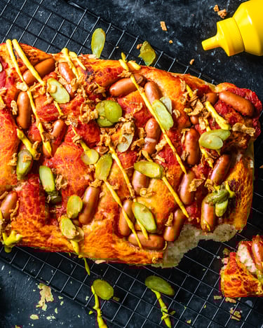 Hot Dog Pizza mit Mini-Würstchen, sauren Gurken, Röstwiebeln und Senf vor dunklem Hintergrund