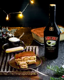 Ein Stück Tiramisu mit Baileys-Creme auf einem Teller, daneben eine Flasche Baileys.