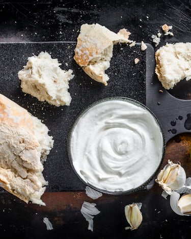 Abgebrochene Stücke vom Ciabatta liegen verteilt um eine Schale mit cremiger veganer Aioli