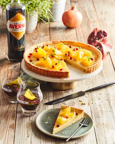 Crostata mit einem Stück auf einem Teller auf Holzuntergrund, dahinter steht eine Flasche Averna und zwei Gläser stehen daneben