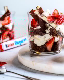 Drei Schicht-Desserts mit Kinder Riegel und Erdbeeren in Gläsern angerichtet in heller Welt