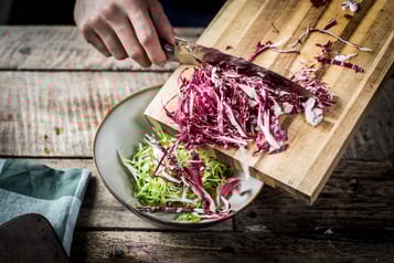 Mithilfe eines Messers wird geschnittener Radicchio in eine Salatschale gegeben