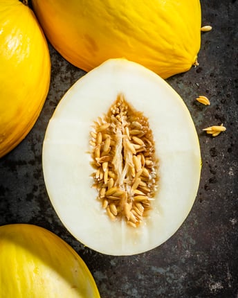 Ganze und halbierte Wintermelonen der Sorte Honigmelone als Topshot von oben auf dunkelgrauem Untergrund