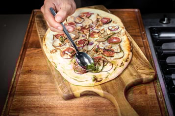 Kräuter werden mit einem Löffel auf dem Flammkuchen verteilt