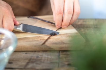Mit einem Messerrücken wird das Mark aus einer Vanilleschote gekratzt