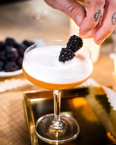 Eine Hand legt einen Spieß mit zwei Brombeeren auf einen French Martini.
