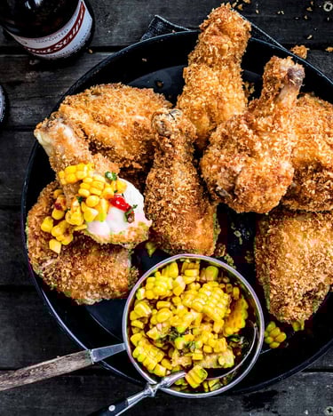 Fried Chicken Wings mit Mais-Chili-Dip in einer Schale neben Bierflaschen auf Holzuntergrund