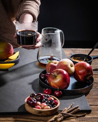 Zur Symbolisierung der fruchtigen Aromen wird der Kaffee in der Glastasse hier zusammen mit frischen Früchten wie Äpfeln, Kirschen und Beeren dargestellt