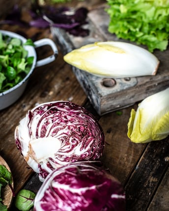 Verschiedene Salatarten, darunter Chicorée, Radicchio, Endivie und Feldsalat liegen zur Weiterverarbeitung auf einem Holztisch
