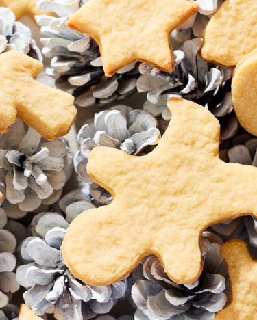 Verschiedene ausgestochene Butterplätzchen liegen auf Tannenzapfen dekoriert