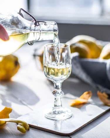 Glas, in das Quittenlikör eingegossen wird, daneben zur Deko Quitten