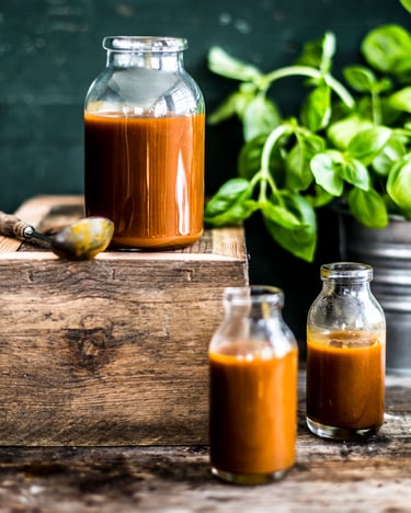 Drei Gläser mit veganer Mango-Burgersauce stehen auf einem Holztisch neben einem Kübel mit frischem Basilikum.