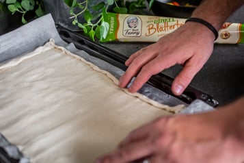 Ein fertiger Blätterteig wird auf einem Backblech ausgerollt