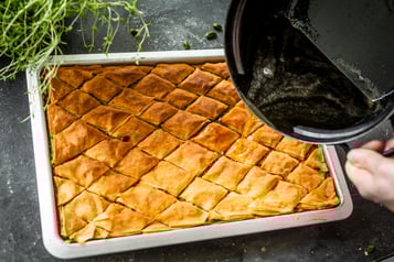 Aus einem Topf wird Honigsirup über frisch gebackene Baklava gegossen.