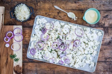 Auf einem Backblech liegen Blumenkohl-Stücke und Zwiebeln