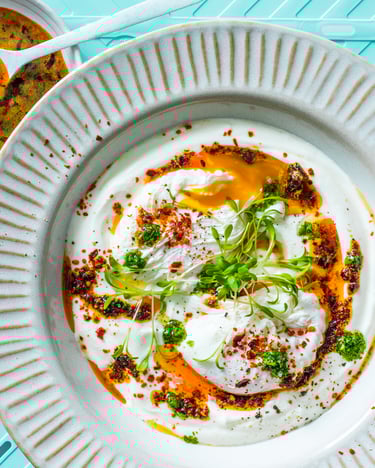 Türkische Eier aufJoghurt mit Chili-Butter und Petersilie vor türkisem Hintergrund