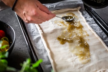Sauce wird mit einem Löffel auf einem Blätterteig verteilt