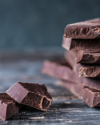 Eine angeschnittene Tafel dunkle Schokolade neben abgebrochenen Schokostücken auf einem Holzuntergrund