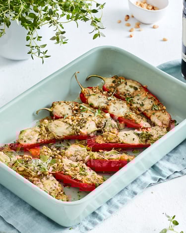 Auflaufform mit gefüllter Spitzpaprika und Kräutern, daneben Balsamico-Essig