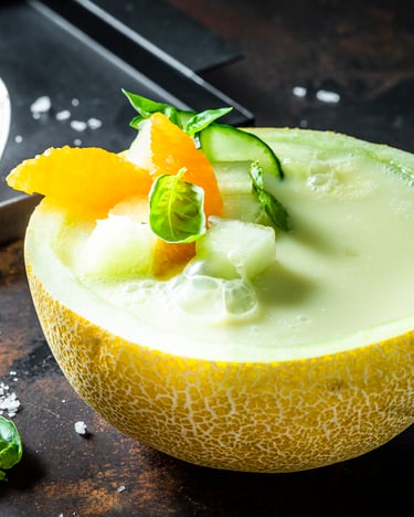 In einer halben Galiamelone ist die Kaltschale serviert und mit Gurken- und Orangenstücken dekoriert.