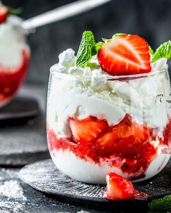 Zwei Glastassen mit einem Dessert aus Sahne, Erdbeeren und Baiser