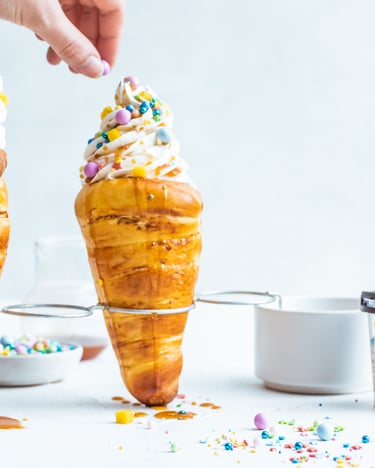 Zwei Chimney Cakes mit Frozen Yoghurt und bunten Zuckerstreuseln vor hellem Hintergrund