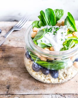 Bulgursalat mit Kichererbsen und Heidelbeeren sowie Feldsalat im Einmachglas neben einer Gabel auf Holzuntergrund