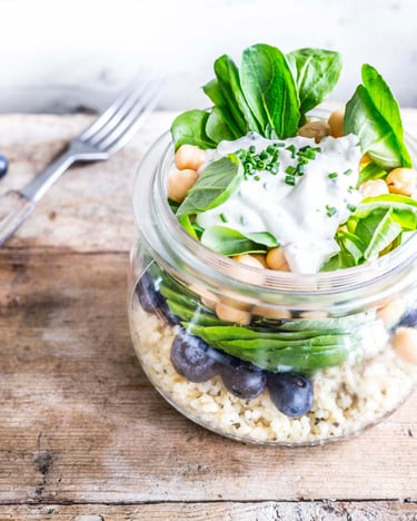 Bulgursalat mit Kichererbsen und Heidelbeeren sowie Feldsalat im Einmachglas neben einer Gabel auf Holzuntergrund