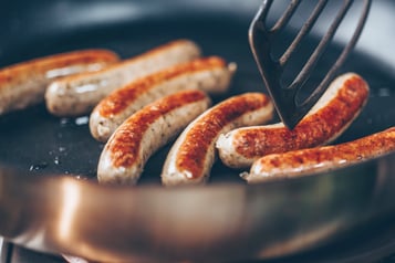 Nürnberger Würstchen werden in einer Pfanne angebraten und mit einem Pfannenwender gedreht