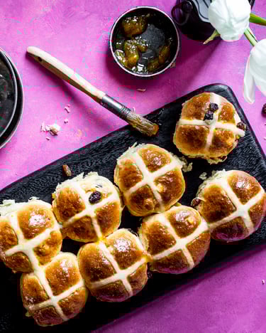 Frische Hot Cross Buns auf schwaren Tellern vor einem pinken Hintergrund
