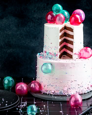 Angeschnittener Bubble Cake mit pinken und türkisen Gelatine-Kugeln vor schwarzem Hintergrund