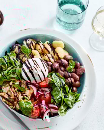 Salat mit Oliven, Gnocchi, Burrata und Balsamico getoppt in tiefem Teller