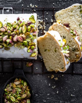 Heller Kuchen aus der Kastenform auf einem Gitter mit Zuckerglasur und Pistazien.
