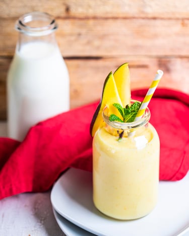 Ein Glas Buttermilch-Mango-Lassi auf einem weißen Teller und einem roten Tuch im HIntergrund