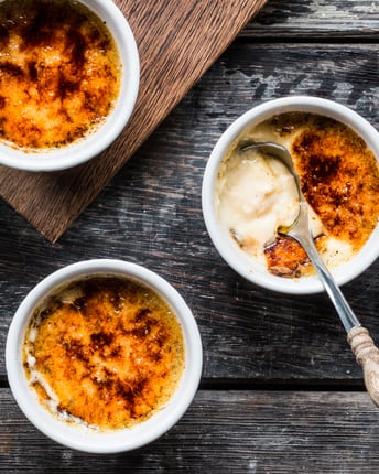 4 Schalen mit Creme Brulee auf dunklem Holz-Untergrund.