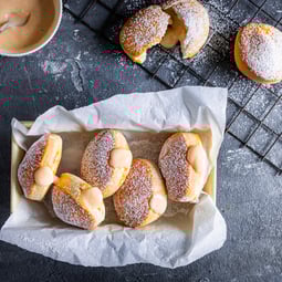 Bomboloni mit Crema pasticcera in einem Korb, der mit Backpapier ausgelegt ist.