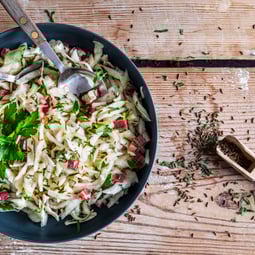 Krautsalat mit Speck in einer Schüssel mit Kümmelsamen auf Holzuntergrund