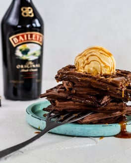 Türkiser Teller mit mehreren Schoko-Waffeln übereinander gestapelt und mit einer Kugel Vanilleis und Baileys-Sauce getoppt.