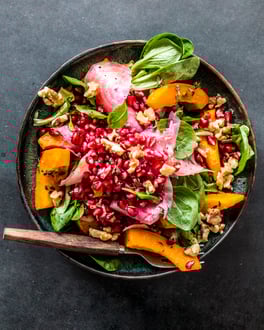 Salat mit Kürbis und Granatapfel von oben fotografiert auf dunklem Untergrund