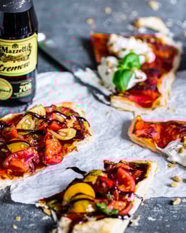 Blätterteig-Pizzette mit Tomaten und Ricotta, daneben eine Flasche Mazzetti Cremoso