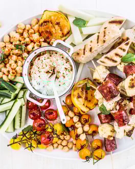 Salatplatte mit viel Gemüse, Brot und Chorizo auf weißem Untergrund mit einer Gabel