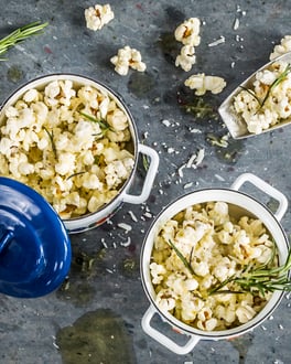 Popcorn mit Rosmarin und Parmesan in zwei kleinen blauen Töpfen auf grauem Untergrund.