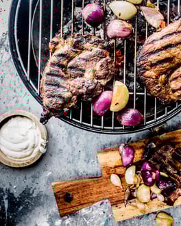 Gegrillte Nackensteaks in Bier-Marinade auf einem Holzbrettchen und dem Grill.