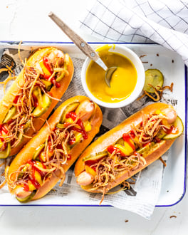 Drei klassische Hot Dogs in weißer Schale angerichtet auf weißem Untergrund