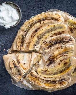 Angeschnittener Banoffee Pie mit Sahne in einem Schälchen auf dunklem Untergrund.
