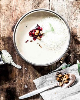 Maronensuppe mit Estragon Senf-Schaum neben grauer Serviette auf Holzuntergrund