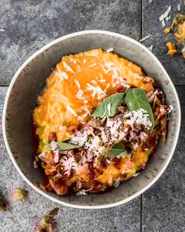 Kürbispüree mit Pancetta, Salbei und etwas geriebenem Käse in einer grauen Schüssel von oben fotografiert.